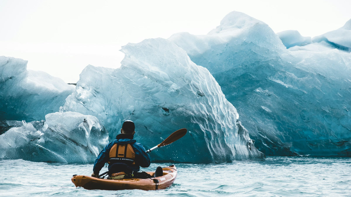 Solo kayaker paddling toward a towering blue glacial iceberg in pristine wilderness