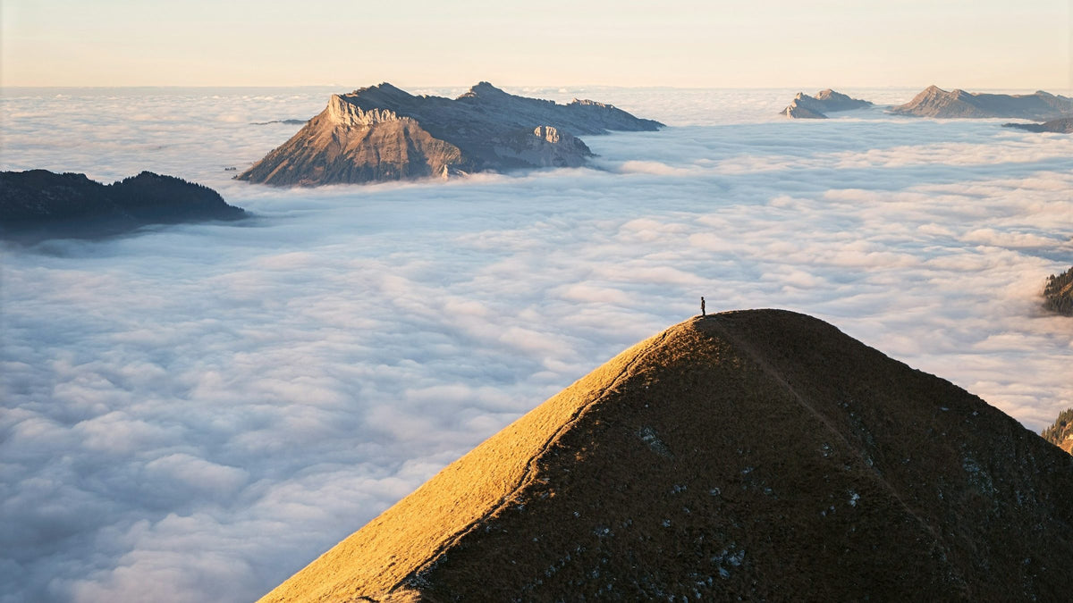 Lone hiker on a golden mountain ridge above a vast sea of clouds at dawn