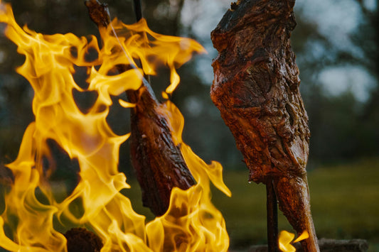Cuts of Patagonian meat roasting on iron stakes over open fire at dusk