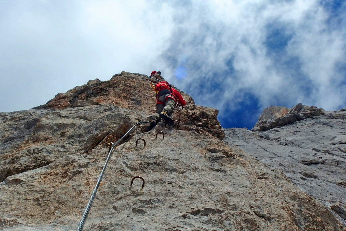 Climber in a harness ascending a via ferrata route with steel cable and iron rungs on a rock face