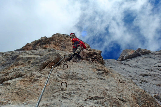 Climber in a harness ascending a via ferrata route with steel cable and iron rungs on a rock face